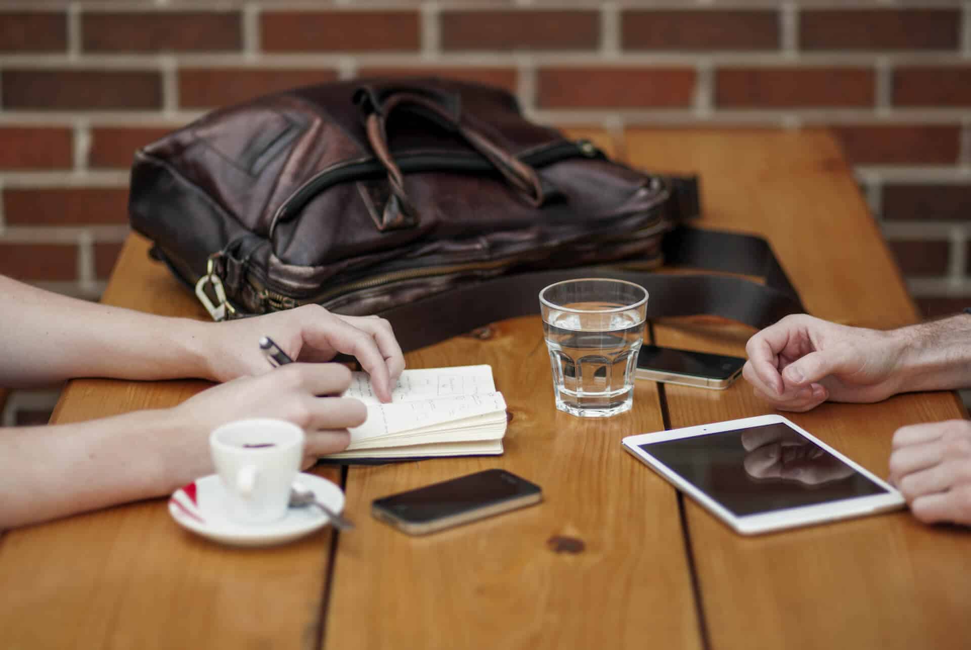 People with iPhone, tablet, coffee and notebook who are writing